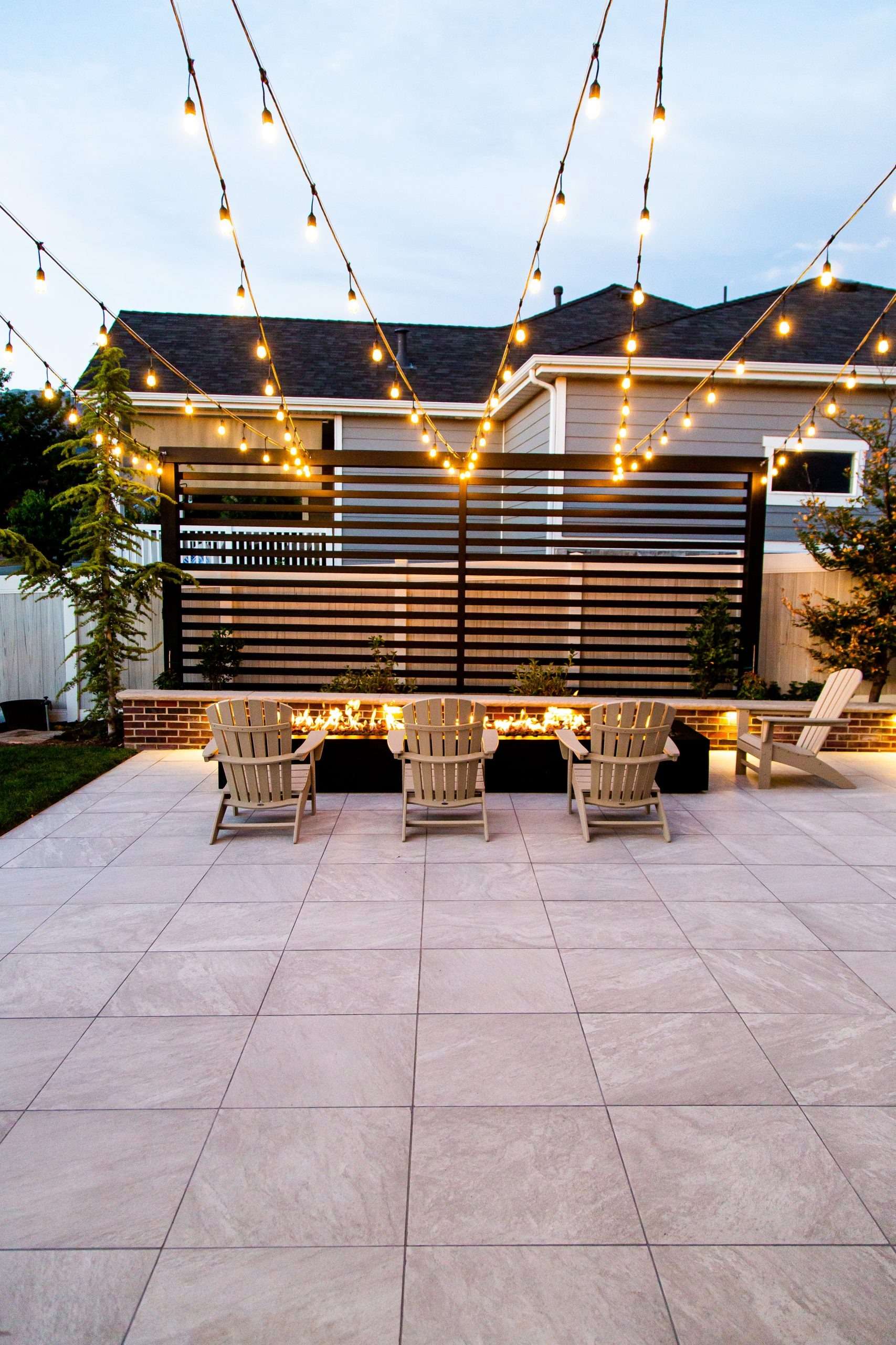 Backyard patio with string lights and fire pit at dusk.